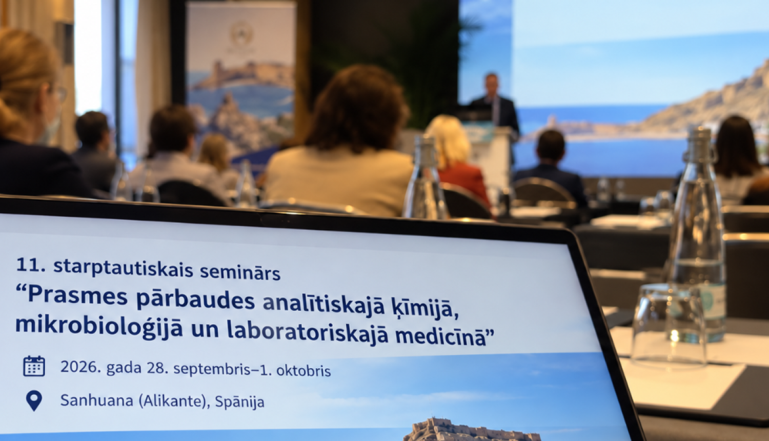 Konferences norise ar dalībniekiem un datoru priekšplānā, kurā redzama informācija par Eurachem semināru par prasmes pārbaudēm analītiskajā ķīmijā, mikrobioloģijā un laboratoriskajā medicīnā.