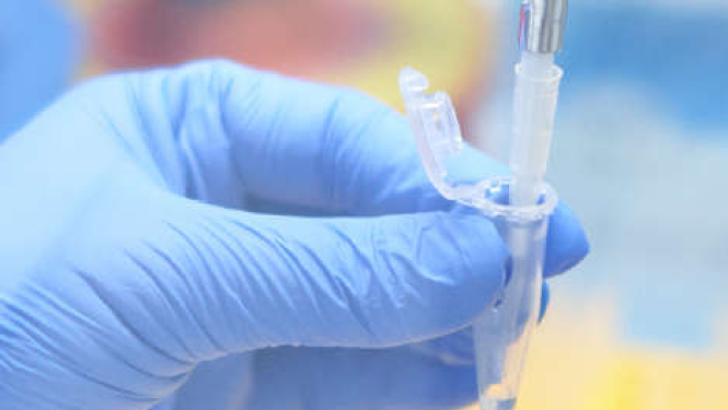 Roka zilā cimdā tur medicīnisko mēģeni