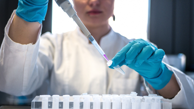 Sieviete tur rokā pipeti un pilda medicīnisku kolbiņu ar šķidrumu