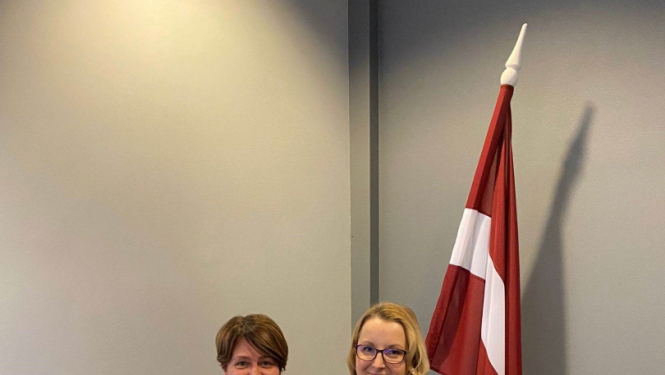 Divas sievietes. Viena tur Izcilības rakstu. Latvijas karogs fonā