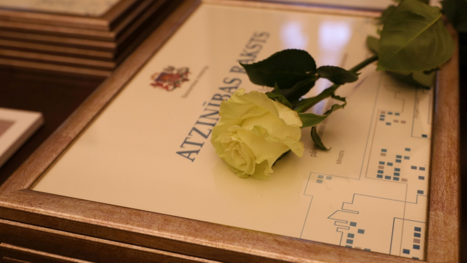 Atzinības raksts koka rāmī ar dzeltenus rozi virsū