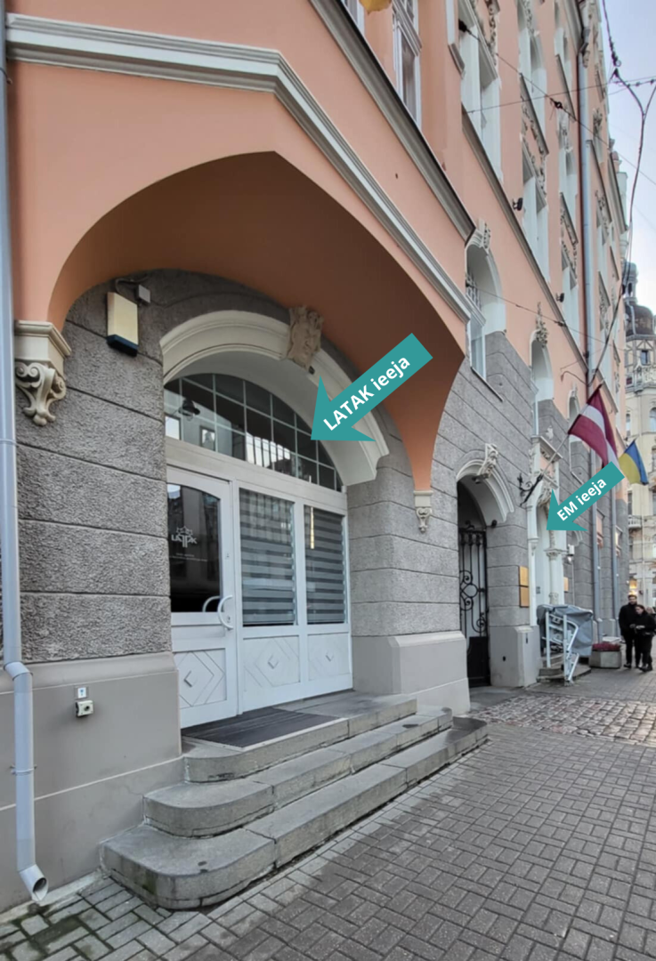 Ekonomikas ministrijas ēka ar 2 ieejas durvīm - vienas baltas, kas ir LATAK ieeja, otras nevar redzēt, bet ir bultiņa, kas norāda, ka tā ir Ekonomikas ministrijas ieeja