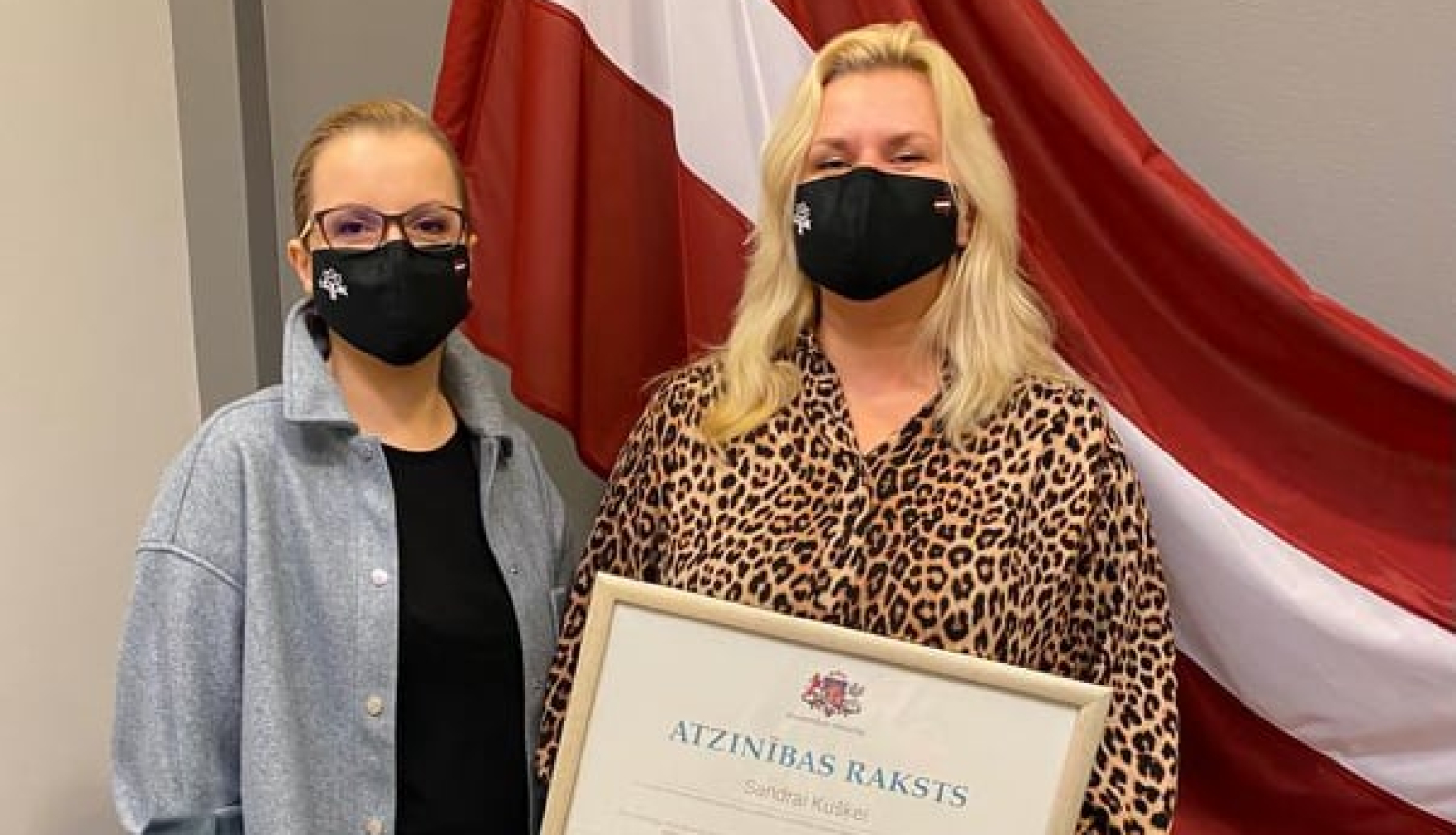 Valsts karogs fonā, LATAK vadītāja un sabiedrisko attiecību speciāliste ar Atzinības rakstu rokās Sandra Kušķe