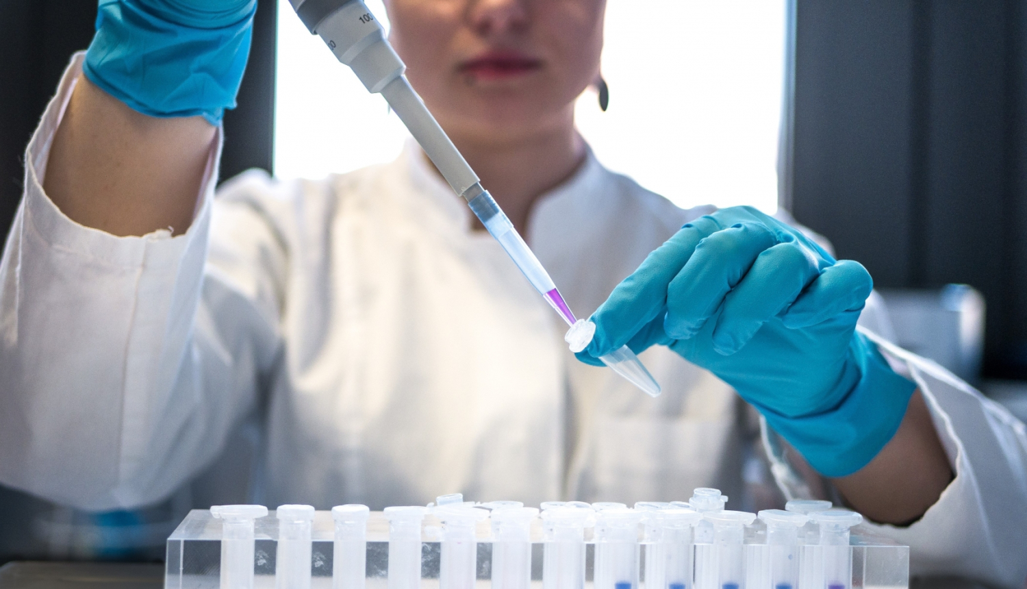 Sieviete tur rokā pipeti un pilda medicīnisku kolbiņu ar šķidrumu