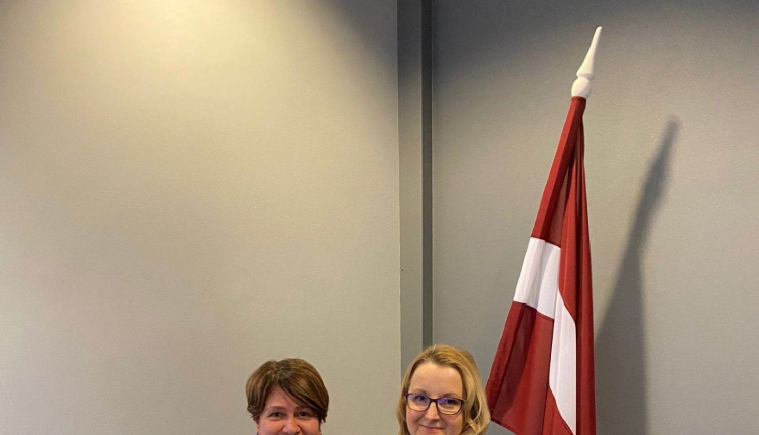 Divas sievietes. Viena tur Izcilības rakstu. Latvijas karogs fonā