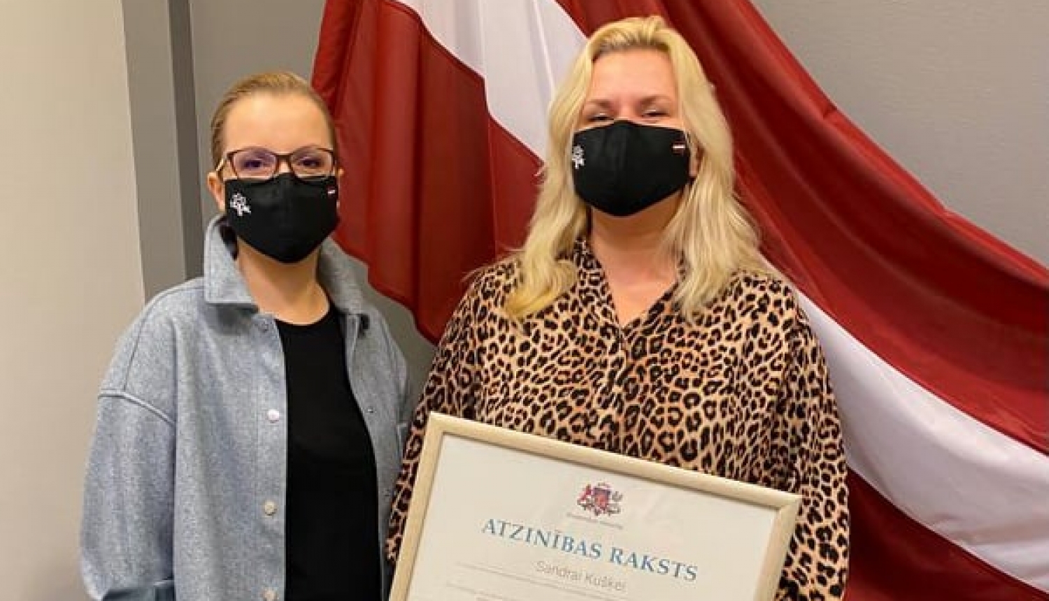 Valsts karogs fonā, LATAK vadītāja un sabiedrisko attiecību speciāliste ar Atzinības rakstu rokās Sandra Kušķe